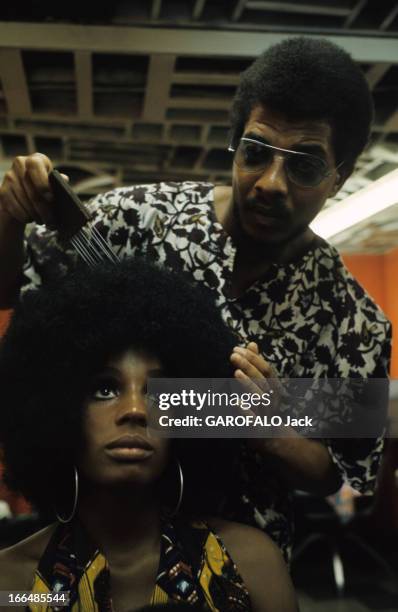 The Ghetto. New York City- Harlemle ghetto; le coiffeur peignant la nouvelle perruque 'dernier cri' de sa cliente, assise, dans le salon de coiffure.
