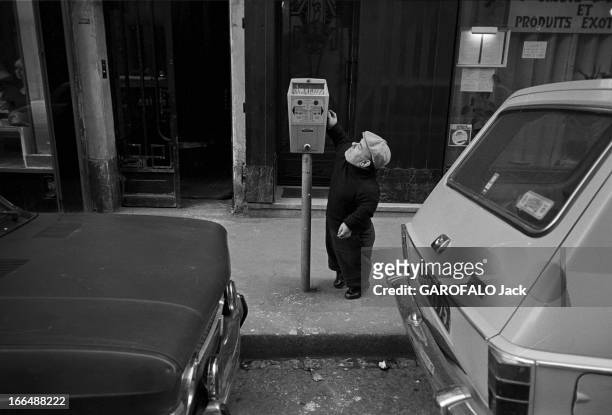 Congress Of Dwarfs In Paris. France, Aubervilliers, 5 avril 1976, Ici sur un trottoir entre deux véhicules, Marcel GUEGAN, un nain âgé de 50 ans, se...