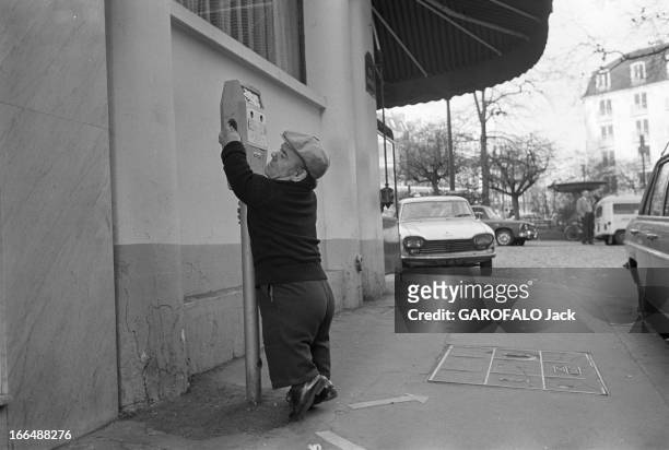 Congress Of Dwarfs In Paris. France, Aubervilliers, 5 avril 1976, Ici sur un trottoir entre deux véhicules, Marcel GUEGAN, un nain âgé de 50 ans, se...