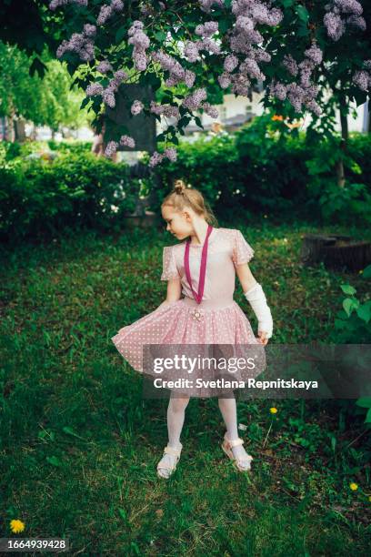 girl gymnast in a pink dress with a plaster cast - agony in the garden stockfoto's en -beelden