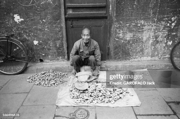 People'S Republic Of China. Shanghai - Octobre 1981 - Dans une rue, portrait d'un marchand installé sur un trottoir, vendant des rhizomes de...