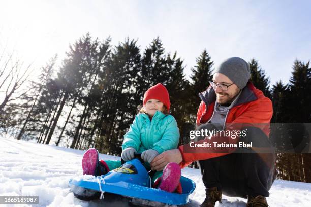 happy girl sledding with father on snow in winter - sled push stock pictures, royalty-free photos & images