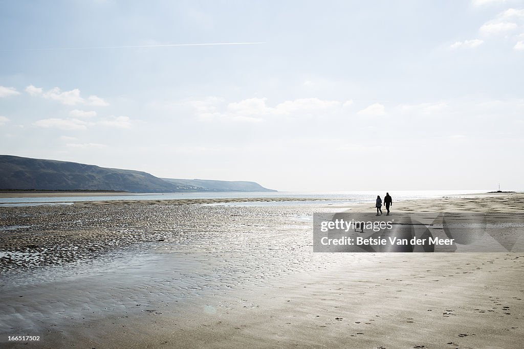Couple walking on beach with dog, North wales.