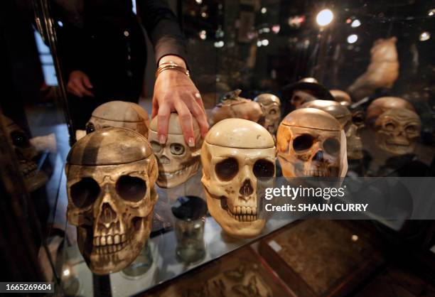 Bonhams employee adjusts a display cabinet containing a collection of ceramic tobacco jars modelled as skulls during a photocall for highlights from...