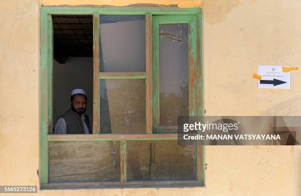 An Afghan election worker looks out of a window as he waits for voters at a polling centre at Baraki Barak district in Logar Province on August 20,...