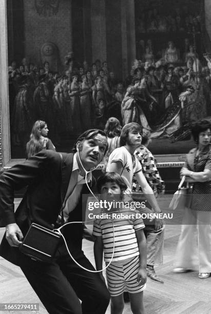 Un enfant et son père admirent une peinture en écoutant un audioguide avec des casques audio dans le musée du Louvre en août 1972 à Paris.