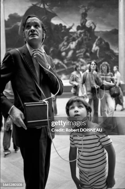 Un enfant et son père admirent une peinture en écoutant un audioguide avec des casques audio dans le musée du Louvre en août 1972 à Paris.