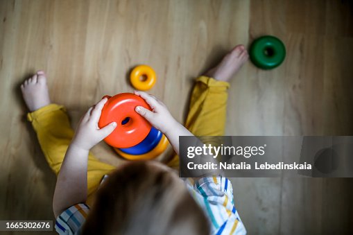 Close-Up Fun: Baby Toddler's Hands Explore Plastic Pyramid on Room Floor.