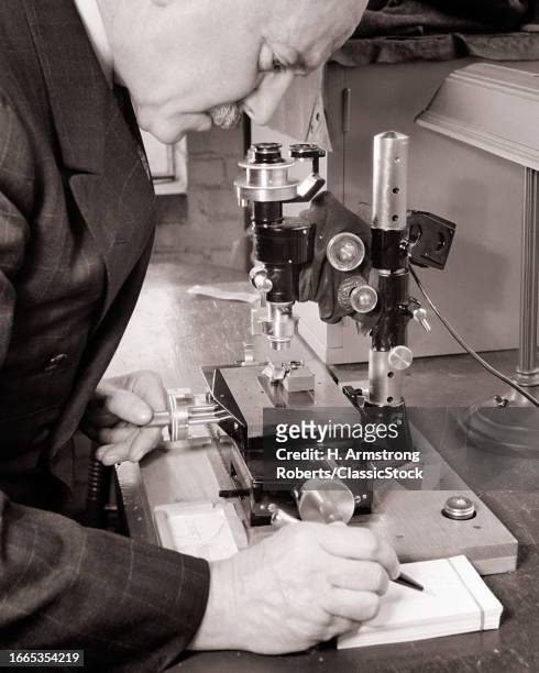 1950s Man research scientist examining specimen under optical microscope in laboratory.