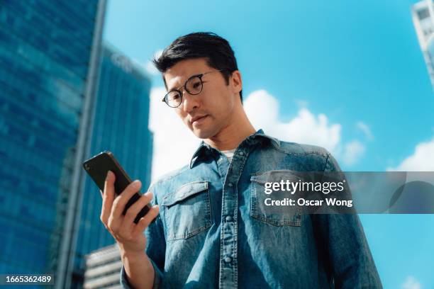 young asian businessman using smartphone against cityscape - banking stock pictures, royalty-free photos & images