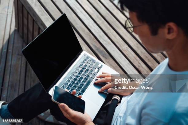 over the shoulder view of young businessman doing finance and investment analysis on smartphone and laptop - digital business london stockfoto's en -beelden