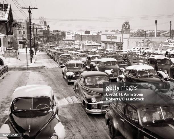 1950s Suburban rush hour traffic jam cars slowed by icy snowy winter roads bumper to bumper.