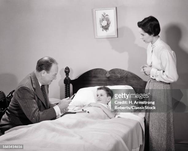 1950s Man doctor making house call with concerned worried mother whose boy son is sick in bed.