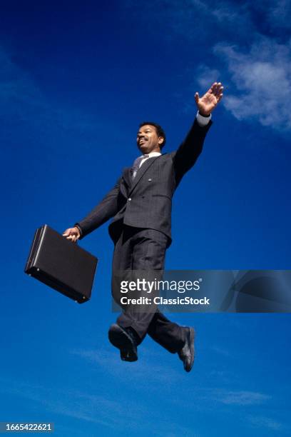 1990s Smiling happy businessman wearing suit and tie jumping in walking on mid air with briefcase.
