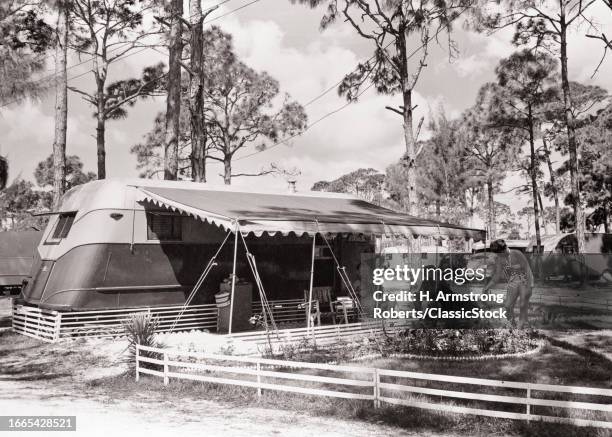 1950s Rv camper with people relaxing under shade awning and flower garden in trailer park camp near sarasota United States USA.