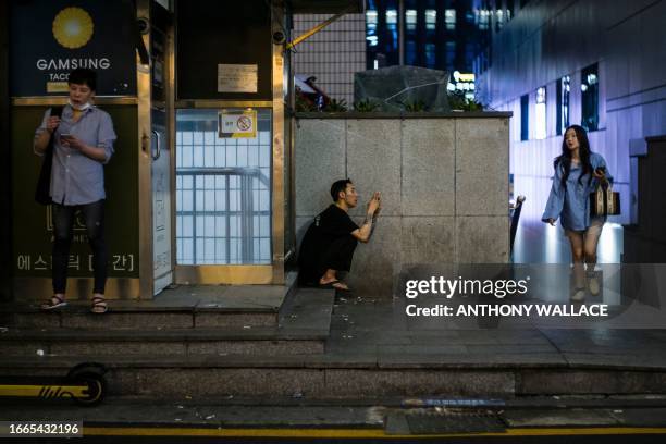 Man crouches as he relaxes on a street in the Gangnam district of Seoul on September 14, 2023. Seoul's Gangnam district, which was made famous by...