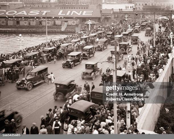 1920s Large diverse crowd of pedestrians on crowded sidewalks and road of a bridge cars parked and also moving traffic.