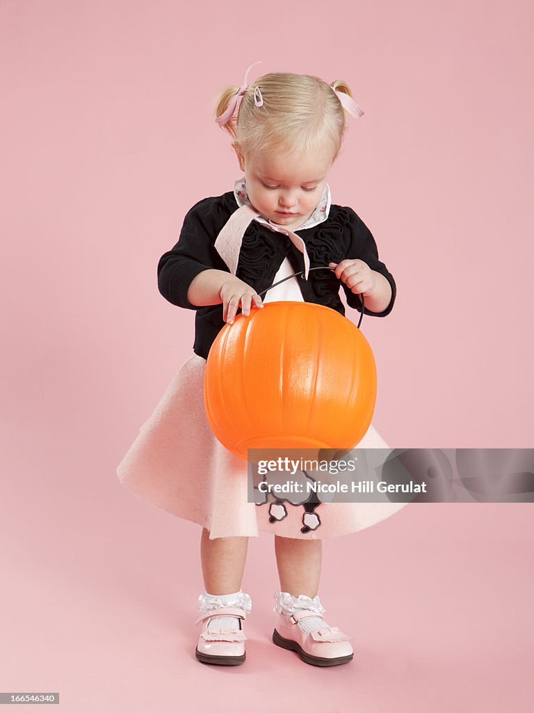 Baby girl (12-17 months) in 1950s style costume, holding pumpkin lantern for Halloween