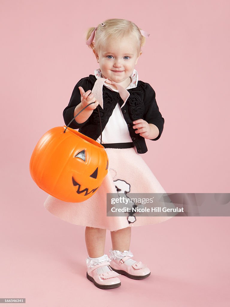 Baby girl (12-17 months) in 1950s style costume, holding pumpkin lantern for Halloween