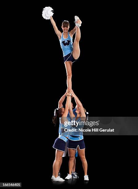 studio shot of cheerleaders (16-17) supporting friend standing on one leg - white pom pom stock pictures, royalty-free photos & images