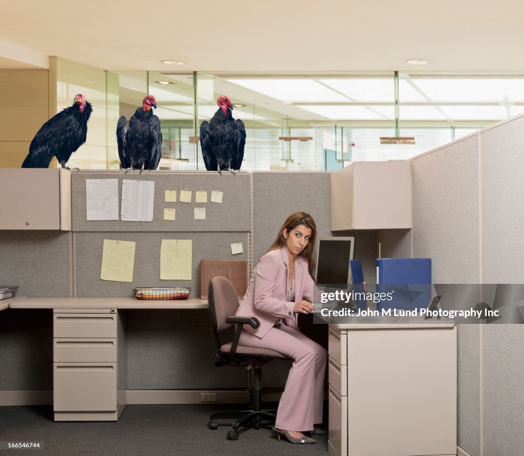 Vultures watching Hispanic businesswoman at desk