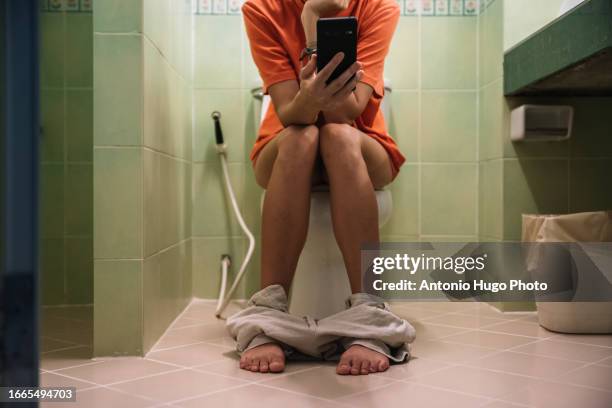 woman sitting on a toilet holding a mobile phone in her hands - urine stock pictures, royalty-free photos & images