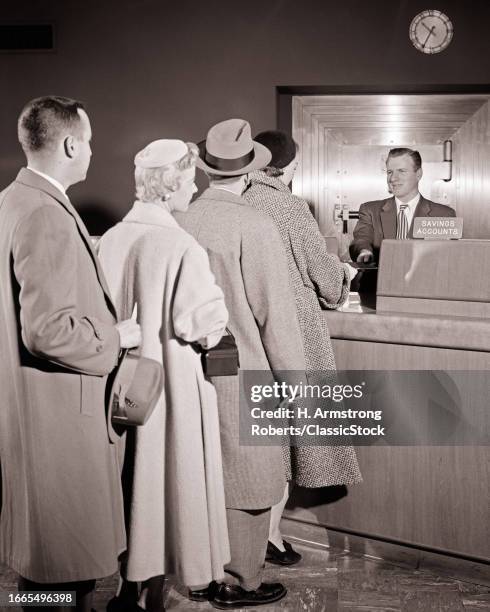 1950s 4 customers two men two women standing in line in bank waiting to see the savings accounts bank teller man behind counter.