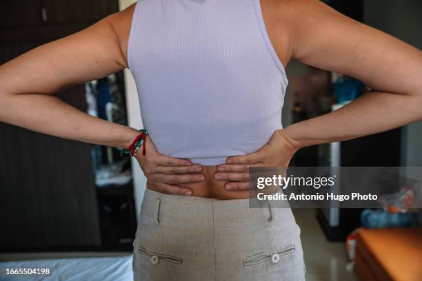 woman touching her back with both hands because she is in pain - lower back stock pictures, royalty-free photos & images