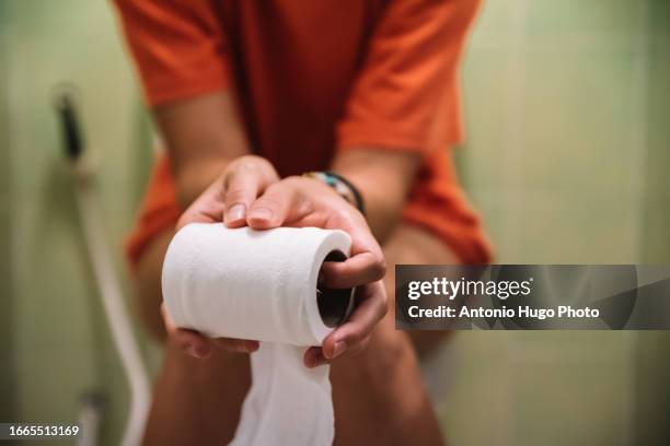 woman sitting on toilet holding toilet paper roll - woman hemorrhoids fotografías e imágenes de stock