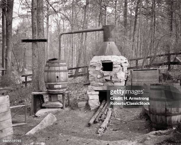 1960s Old time hillbilly moonshine still in woods stone fireplace copper kettle that distills into wooden barrel.