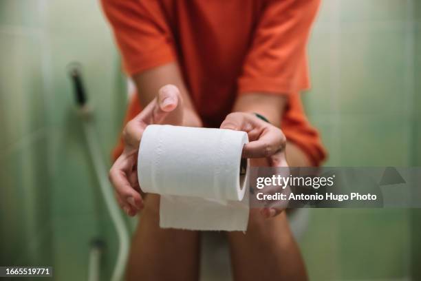woman sitting on toilet holding toilet paper roll - banheiro-feminino imagens e fotografias de stock