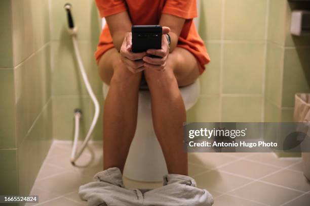 woman sitting on a toilet holding a mobile phone in her hands - human toilet stock-fotos und bilder
