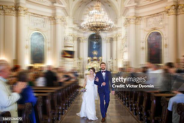 young newlyweds walk out from the church full of guests - altar stock-fotos und bilder