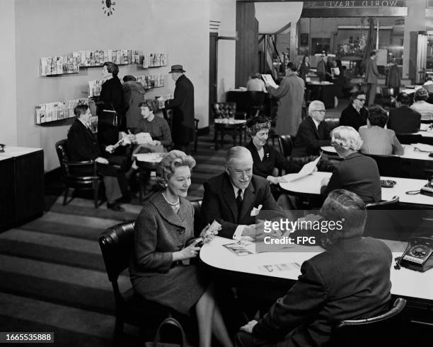 Group of people sit speaking with agents in the offices of the American Express World Travel Service, on Fifth Avenue in New York City, New York,...
