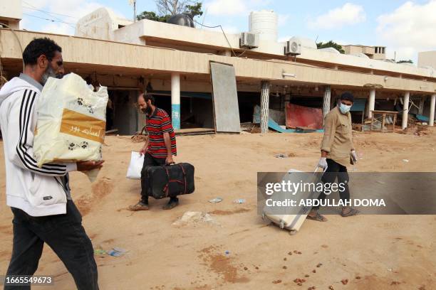 People carry some of their belongings as they walk along a muddy street following flash floods in Libya's eastern city of Derna, on September 14,...