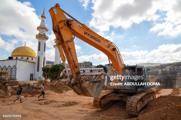 Men walk past a mosque and an earthmover in a flash flood-damaged area in Derna on September 14, 2023. A global aid effort for Libya gathered pace on...