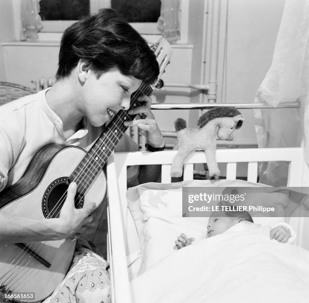 Close-Up Of Cecile Aubry And Son Mehdi. En France, en juin 1956, dans une chambre, portrait de Cécile AUBRY les cheveux courts, jouant de la guitare...