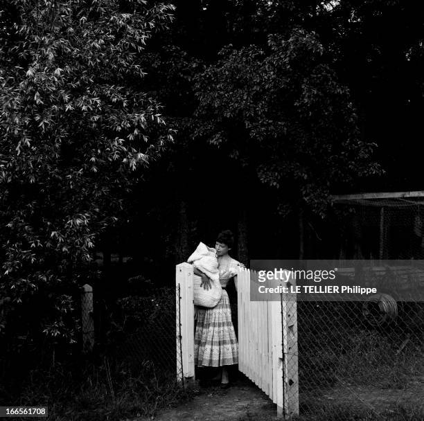 Close-Up Of Cecile Aubry And Son Mehdi. En France, en juin 1956, portrait de Cécile AUBRY les cheveux courts, ouvrant un portail dans un jardin, avec...