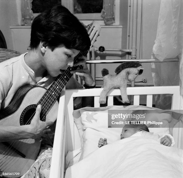 Close-Up Of Cecile Aubry And Son Mehdi. En France, en juin 1956, dans une chambre, portrait de Cécile AUBRY les cheveux courts, jouant de la guitare...