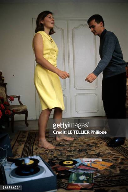 Close-Up Of Guyonne Slab. Neuilly-sur-Seine - 1963 - La skieuse nautique Guyonne DALLE chez elle, en robe jaune, dansant face à son frère près d'un...