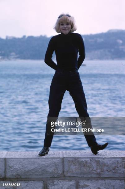 Rendezvous With Mireille Darc. En France, en 1966, Mireille DARC, en pantalon et pull col roulé, posant debout sur un muret sur fond de mer.