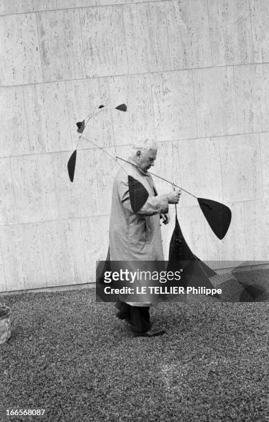 Sculptor Alexander Calder Makes A Mobile For The Palace Of Unesco. A Paris, devant le palais de l'UNESCO, Alexandre CALDER, en imperméable, tenant...