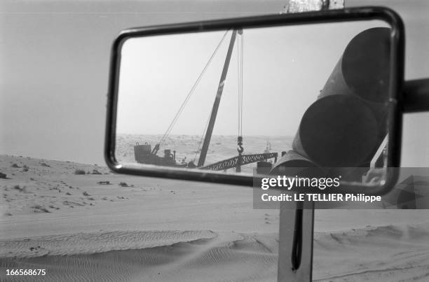 Construction Of Pipe Line. En 1958, dans le désert du Sahara, vue dans le rétroviseur d'un camion, d'un engin de levage et de troncons de...