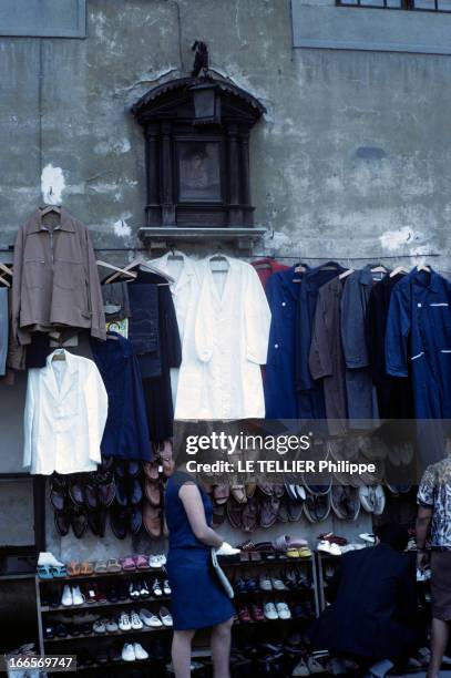 The City Of Florence, Italy. Florence - juin 1967 - Dans une rue, des chaussures et des vêtements d'une boutique accrochés à un mur, sous un ex-voto,...