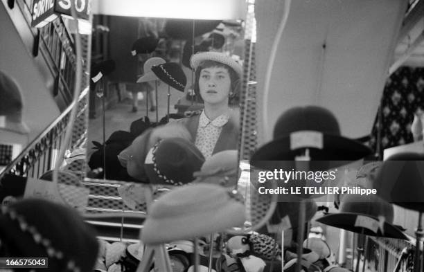 Young Girl Diverted. 1955, le 7 juin, portrait d'une jeune fille faisant des achats dans des boutiques : au rayon des chapeaux, un miroir renvoie son...