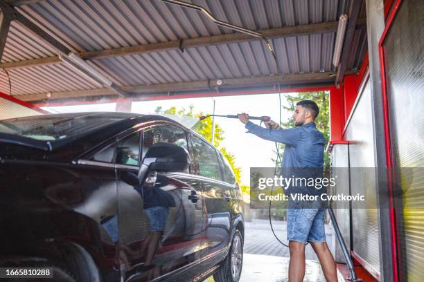 young man washing his car at a self-service car wash using a hose with pressurized water - car splashing water on people stock pictures, royalty-free photos & images