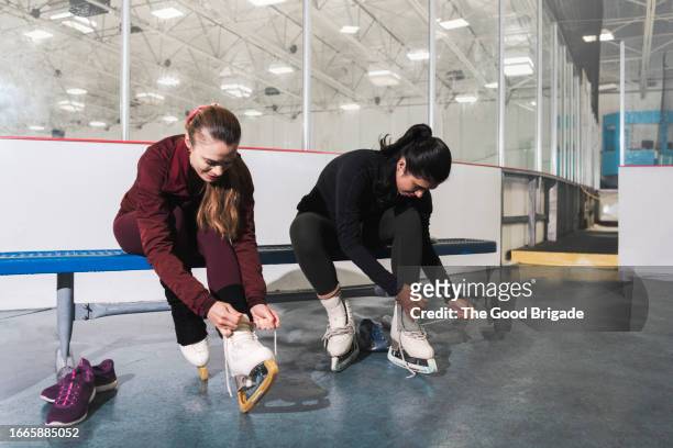 female friends tying shoelaces on ice skates - learning to ice skate stock pictures, royalty-free photos & images