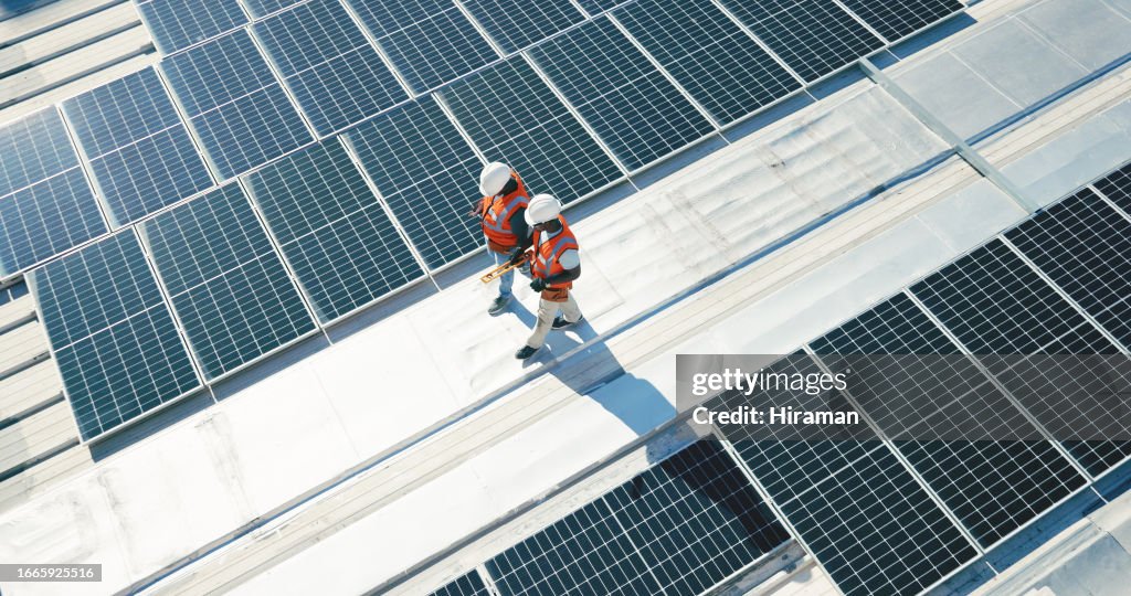Renewable energy, solar panels and team walking on roof planning for inspection at sustainable business. Engineering, sustainability and photovoltaic power, men in electricity maintenance from above.