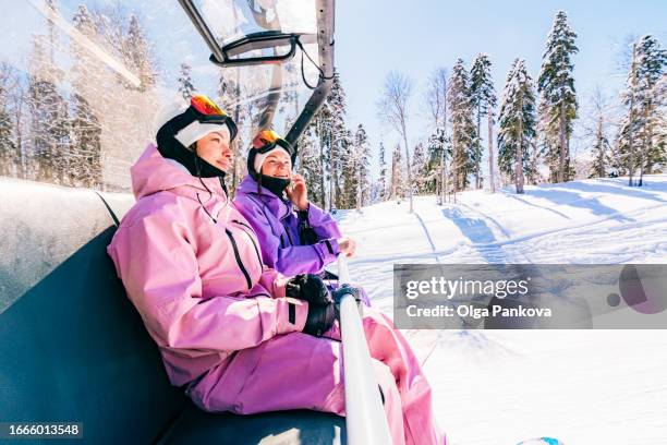 female snowboarders friends on a mountain chairlift while snowboarding on a sunny day - skifahren und snowboarden stock-fotos und bilder