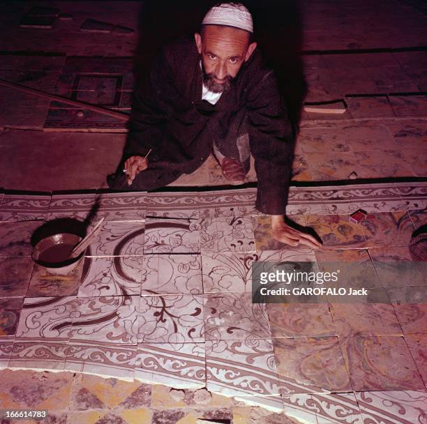 The Iranian Rugs. En Iran, vue en plongée d'un homme coiffé d'une chéchia, accroupi sur le sol un pinceau à la main, dessinant des motifs sur du...